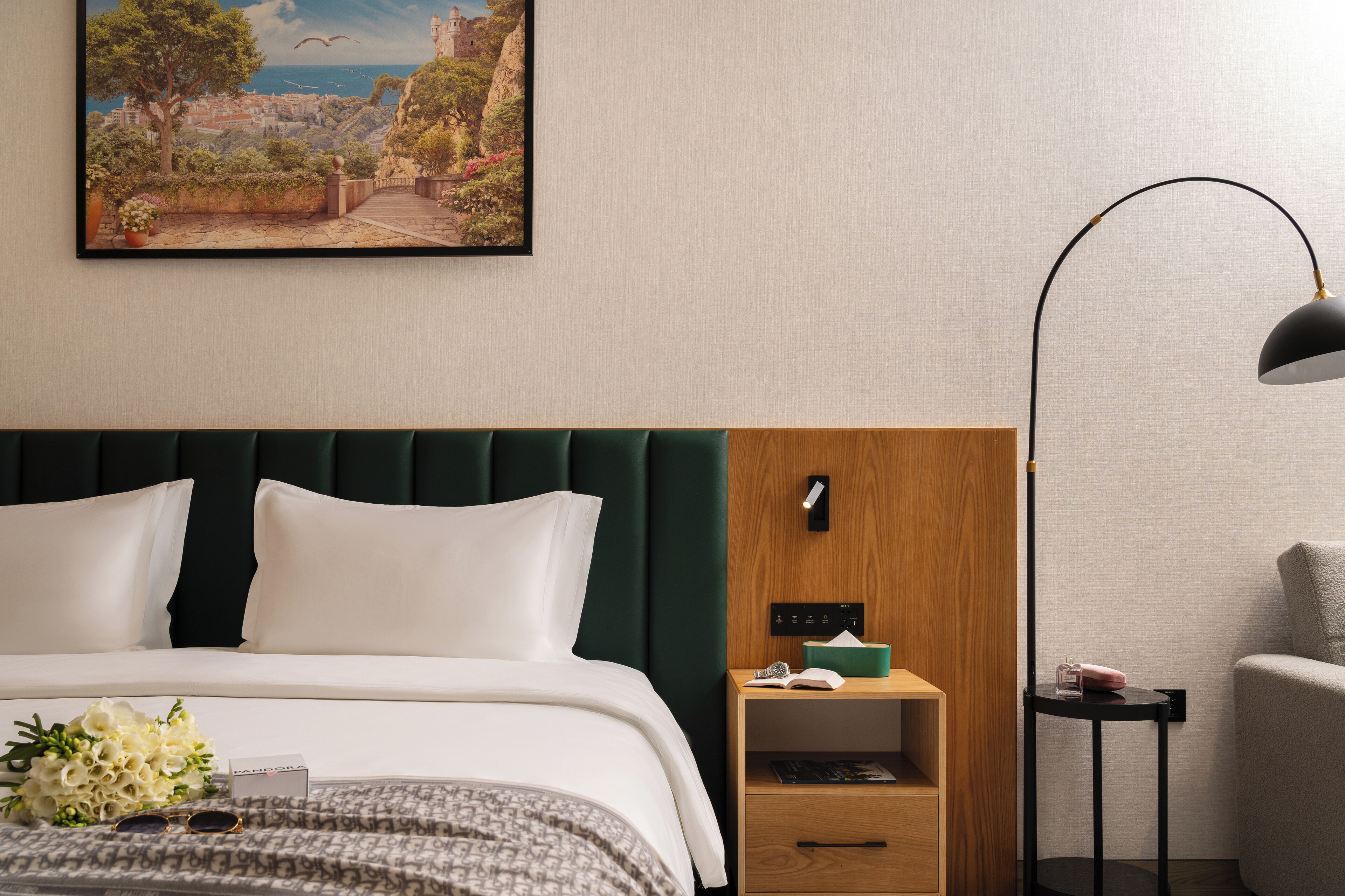 Une chambre d’hôtel avec un lit, une table de chevet, une lampe et un tableau représentant un paysage pittoresque.