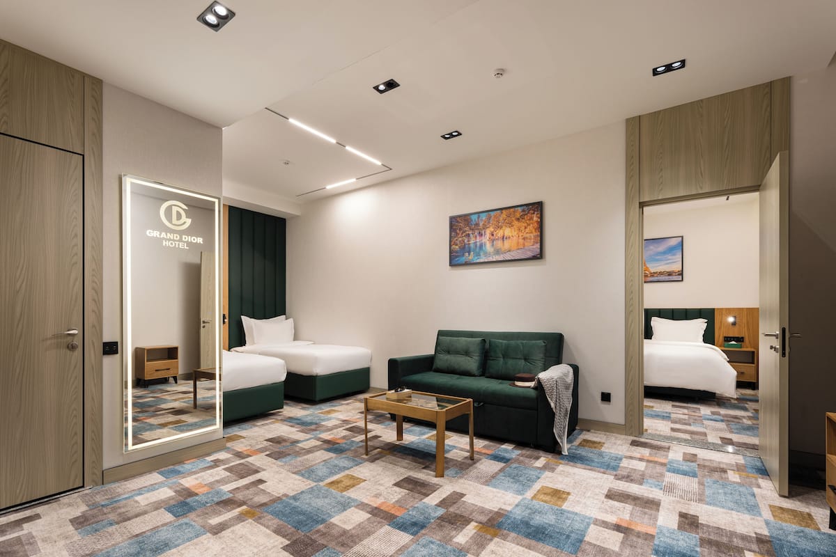 A hotel room with a large mirror, two beds, a green sofa, a coffee table, and a colorful carpet.