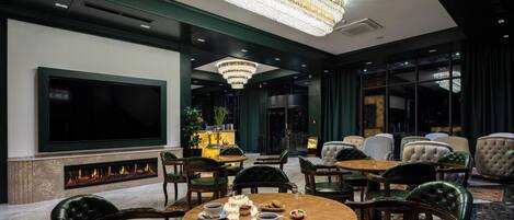 A spacious lobby with a large flat-screen TV, a fireplace, comfortable seating, and a chandelier.
