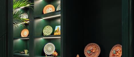 A hallway with dark green cabinets, shelves with decorative plates, and a marble floor.