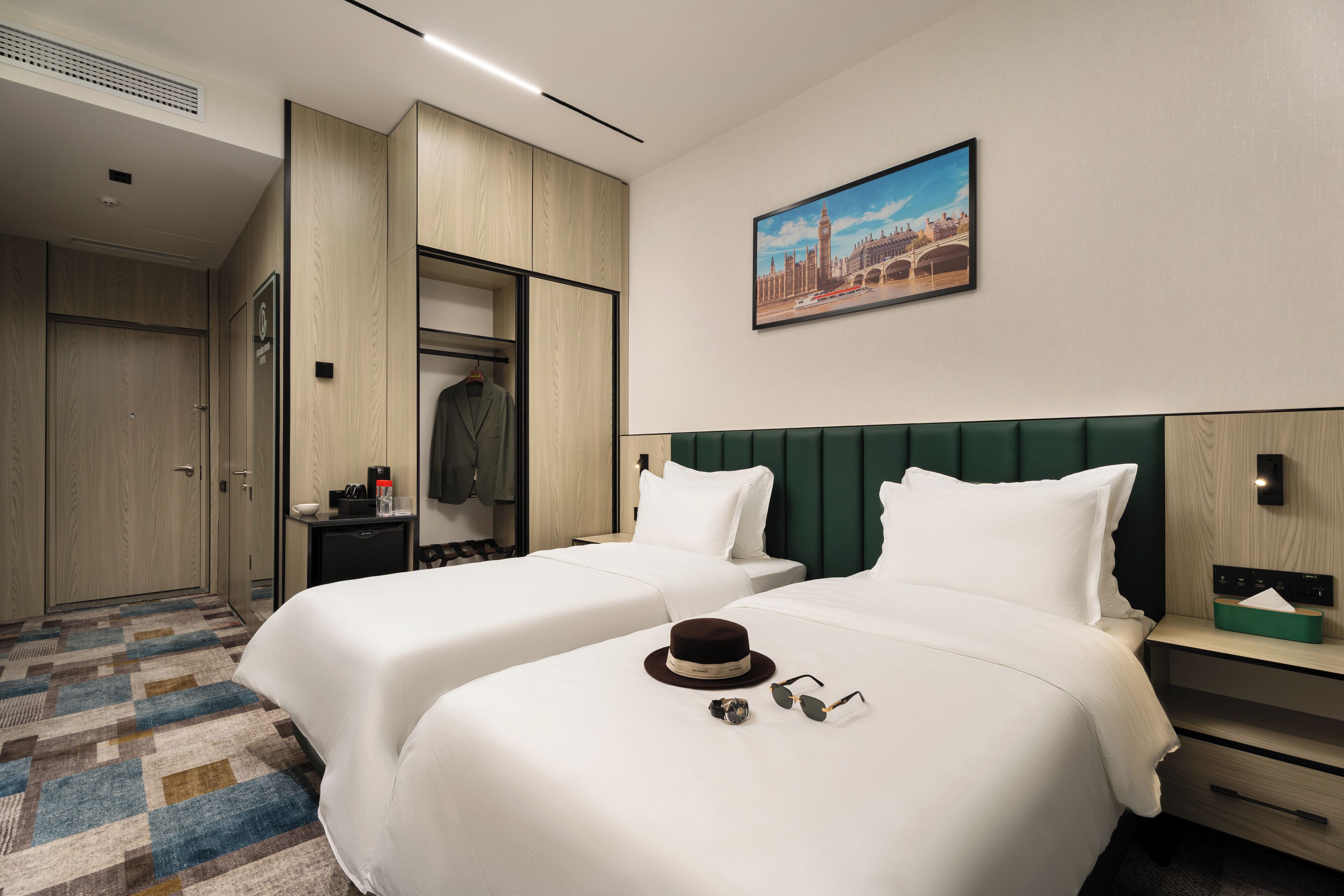 Ein Hotelzimmer mit zwei Betten, einem Kleiderschrank, einem Schreibtisch und einem Stadtbild.