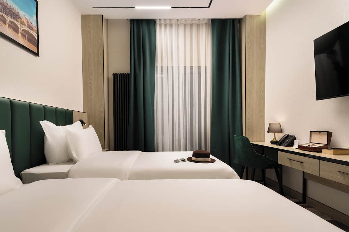 A hotel room with two beds, a desk, a chair, a television, and a window with curtains.