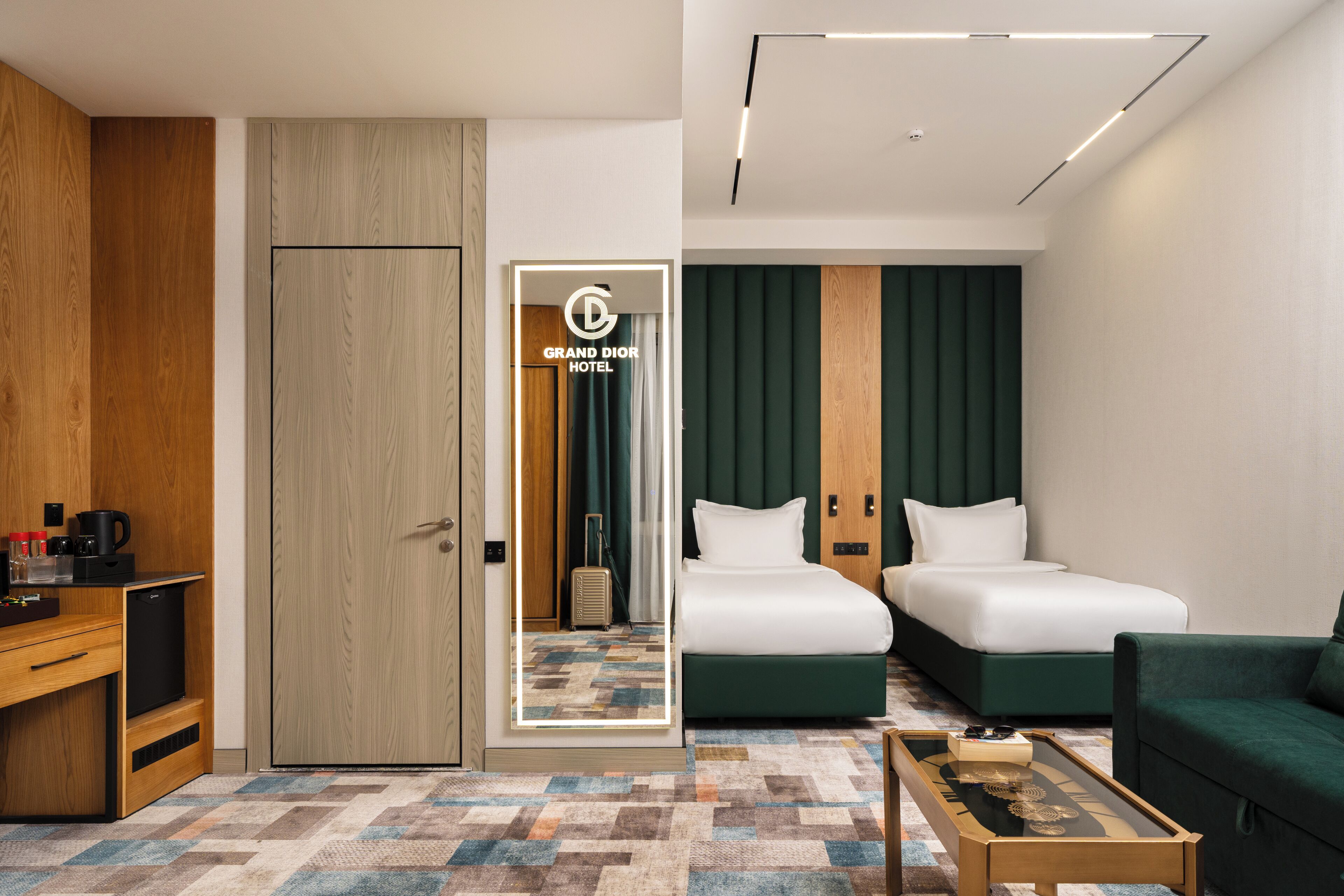 Habitación de hotel con dos camas, un escritorio, una cafetera y un espejo con el nombre del hotel.