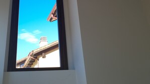 Une fenêtre donnant sur le toit d’un immeuble, avec un panneau indiquant l’emplacement d’un extincteur sur le mur.