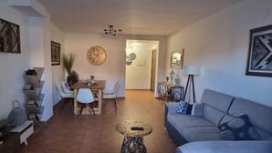 Un salon comprenant un canapé, un téléviseur, une table à manger, des chaises et une horloge au mur.