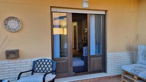 Un espace patio avec une porte-fenêtre coulissante donnant sur une pièce, un banc en bois et une petite table.