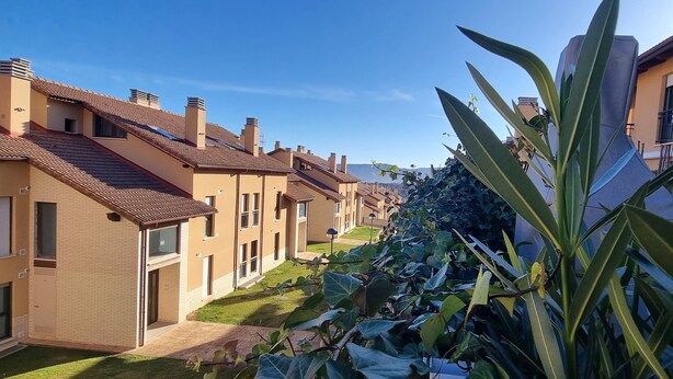 Une rangée d’immeubles résidentiels à l’architecture uniforme, un ciel dégagé et une pelouse bien entretenue.