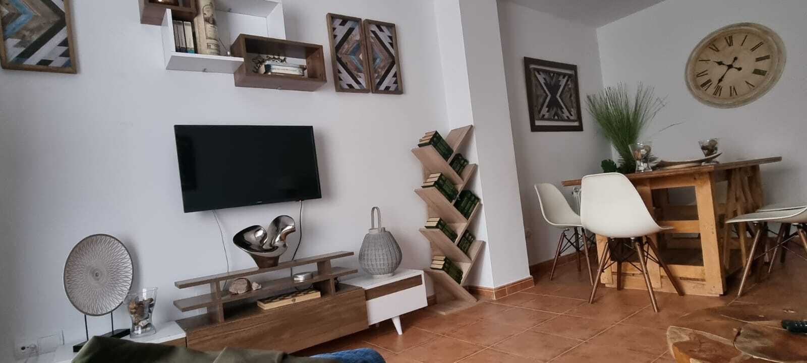 Ein Wohnzimmer mit Flachbildfernseher, Couchtisch, Bücherregal und einem Essbereich mit Stühlen und Tisch.