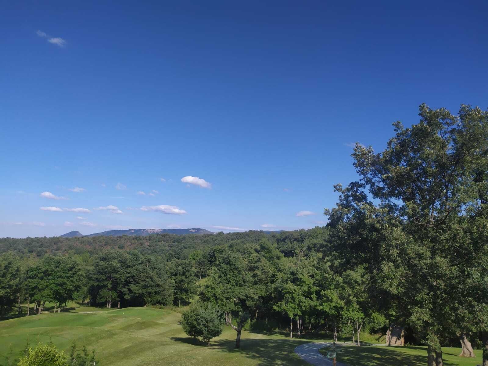 Ein Golfplatz mit blauem Himmel, üppigem Grün und Bergen in der Ferne.