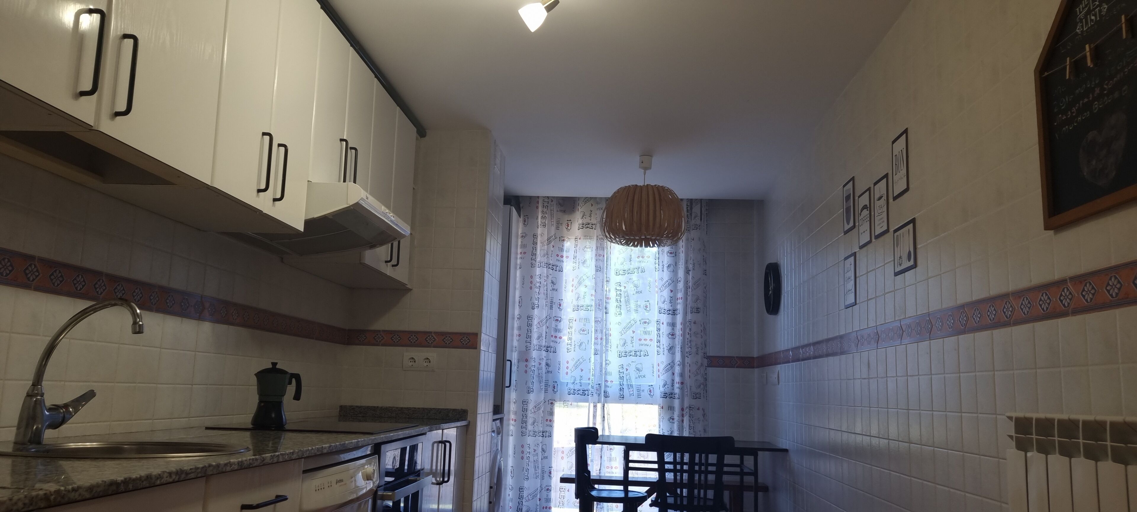 Una cocina con armarios blancos, un lavabo y una ventana con cortinas estampadas.