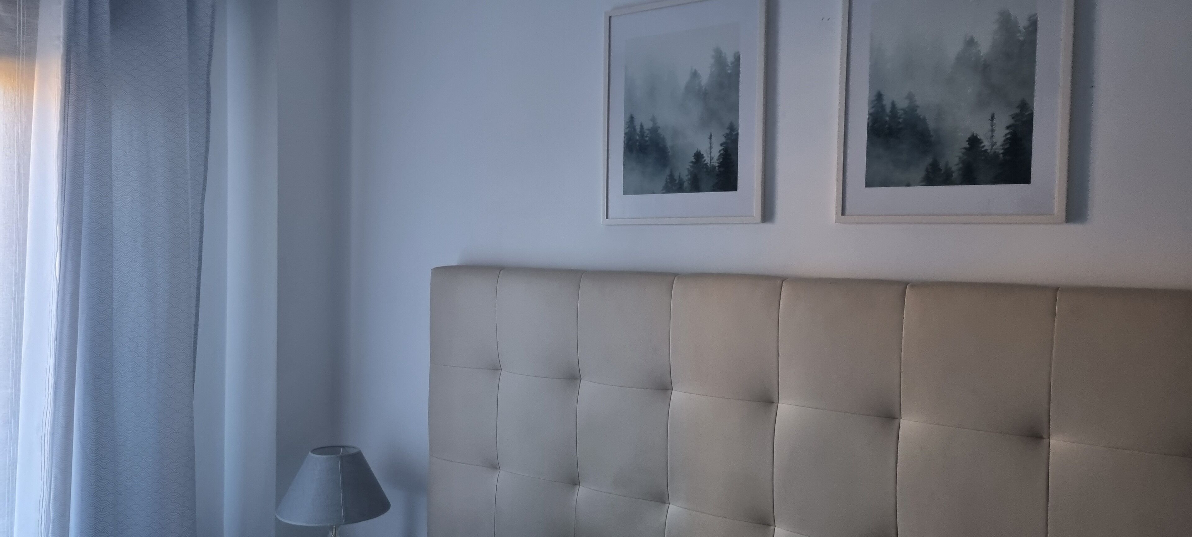 Un dormitorio con un cabecero capitonado, una lámpara de noche y dos cuadros en la pared.