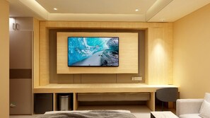 Un soggiorno moderno con una grande TV a schermo piatto montata su una parete in legno, una zona salotto con un divano e una poltrona, e un piccolo cestino.