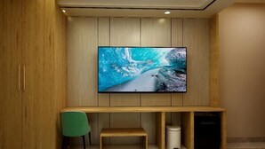 Una habitación moderna con una amplia televisión de pantalla plana montada en una pared de madera, una silla verde, un banco de madera y un mueble bajo la televisión.