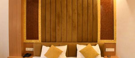 A hotel room with a large bed, two bedside tables, a wooden headboard, and a wall-mounted air conditioning unit.