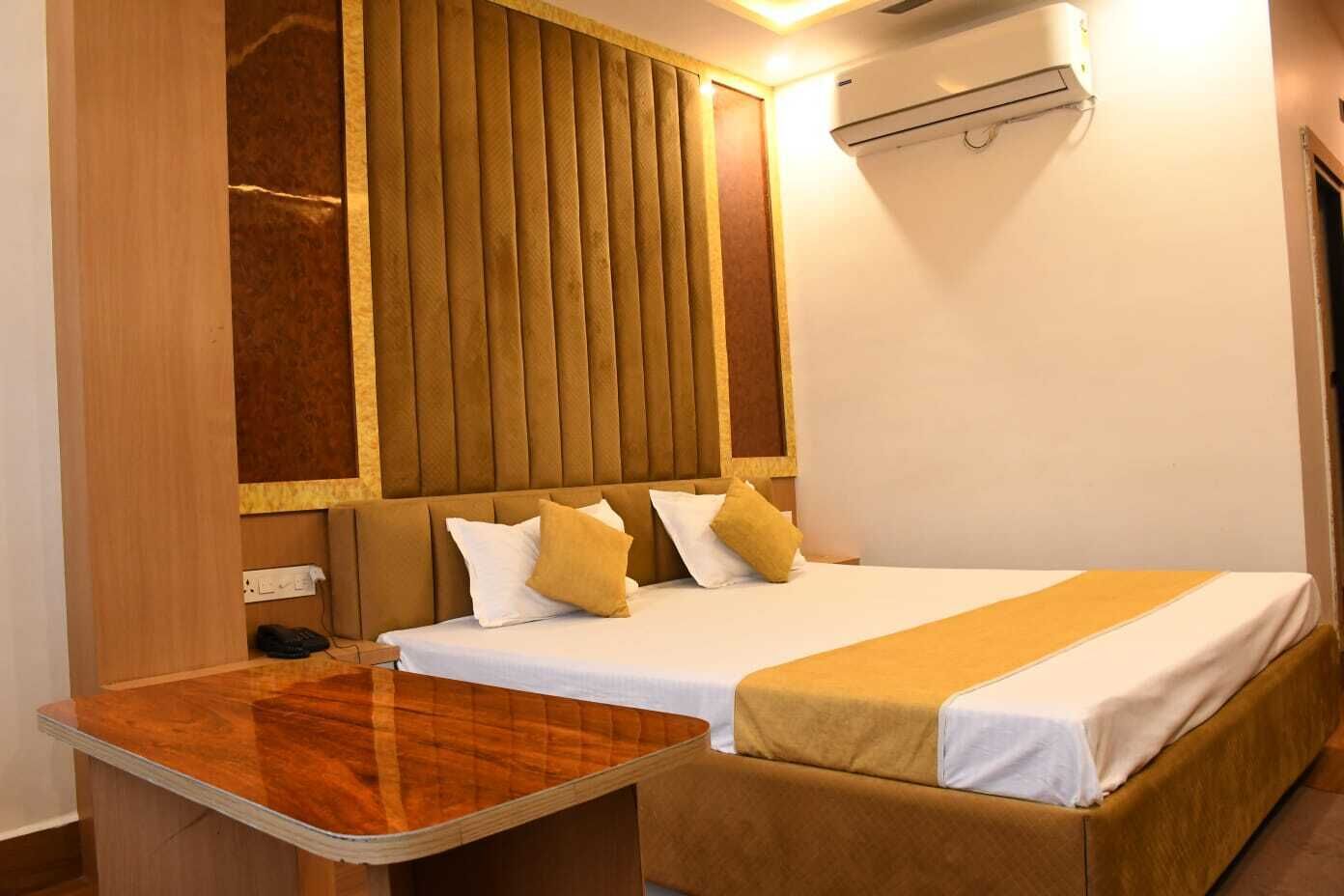 A hotel room with a bed, bedside table, and an air conditioning unit.