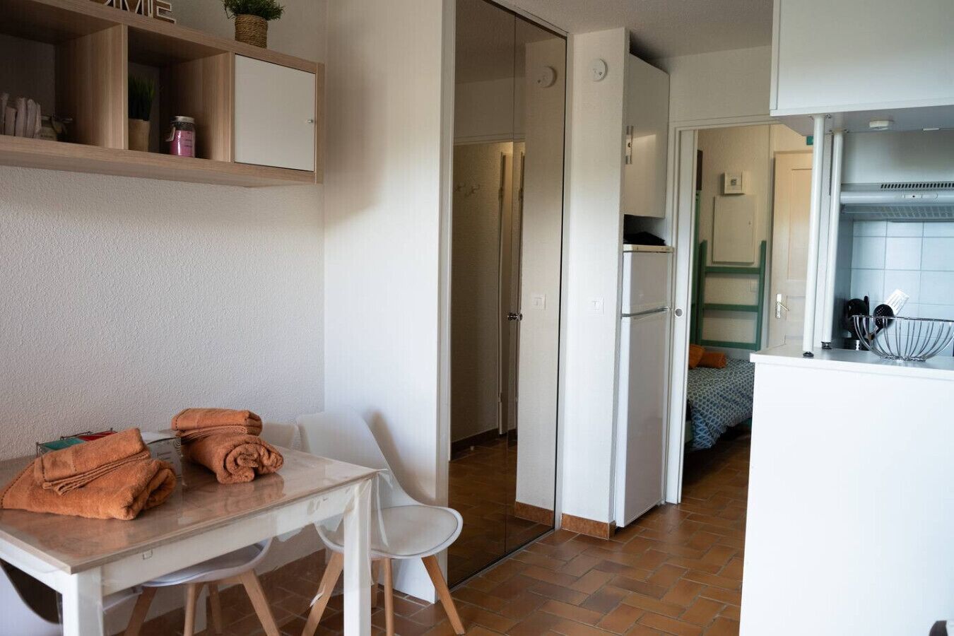 A compact kitchen with a refrigerator, a dining area with a table and chairs, and a small cabinet with items on it.