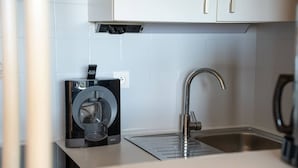 A modern kitchen with a built-in coffee maker, a stainless steel sink, and white cabinets. - Alora - Studio Vue Mer Climatisé avec Piscine (Cavalaire-sur-Mer)