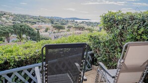 A terrace with two chairs overlooking a scenic view of a town with buildings and trees. - Alora - Studio Vue Mer Climatisé avec Piscine (Cavalaire-sur-Mer)
