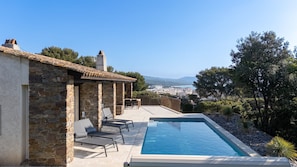 A pool with lounge chairs, a stone building, and a view of a town. - Villa Perlazur - Piscine & Vue Mer, Calme et Luxe (Cavalaire-sur-Mer)