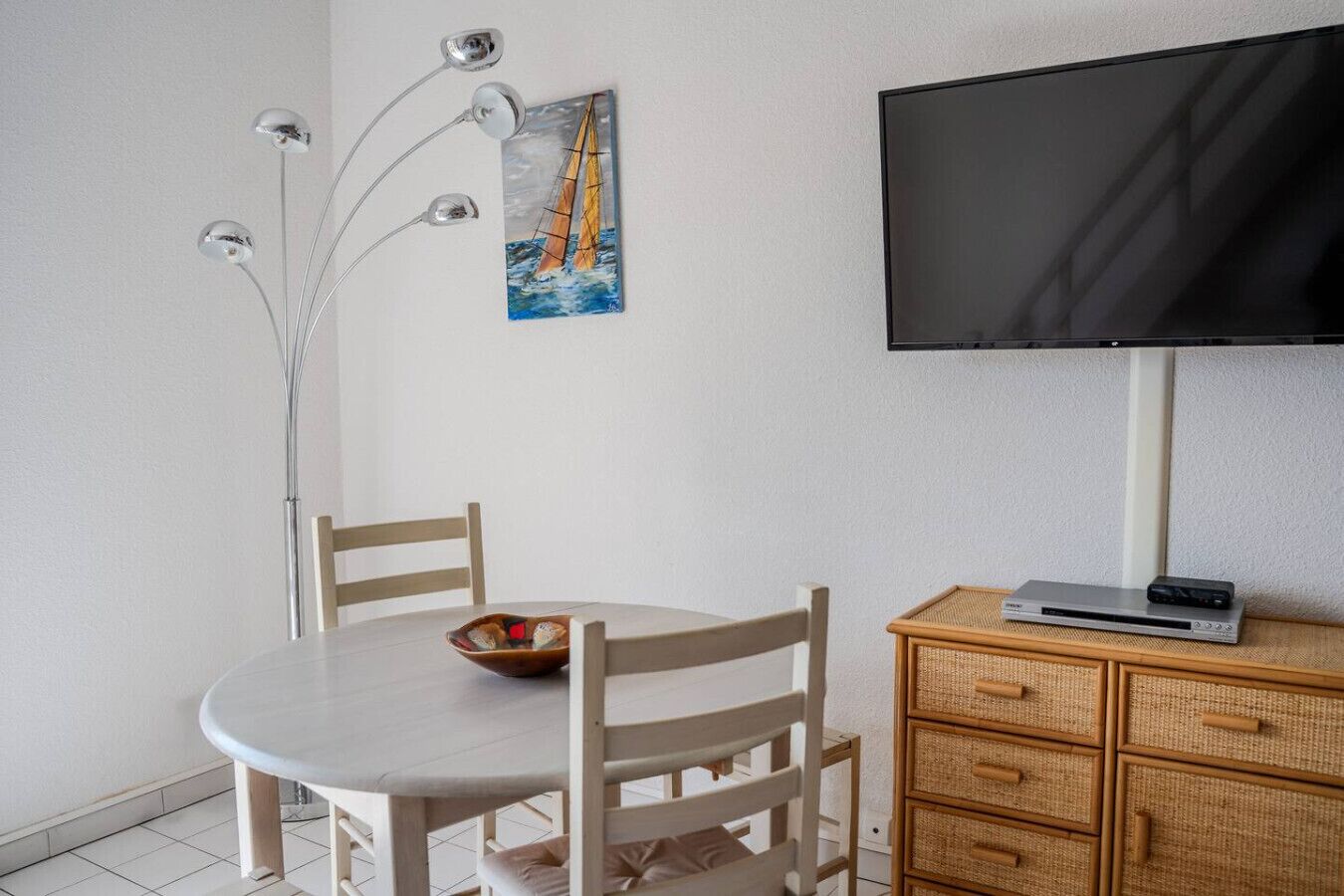 Huone, jossa on ruokapöytä, tuoleja, televisio ja koristeellinen taulu.