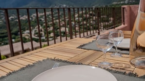 A table set with a plate, two wine glasses, and a pitcher, overlooking a mountainous landscape.