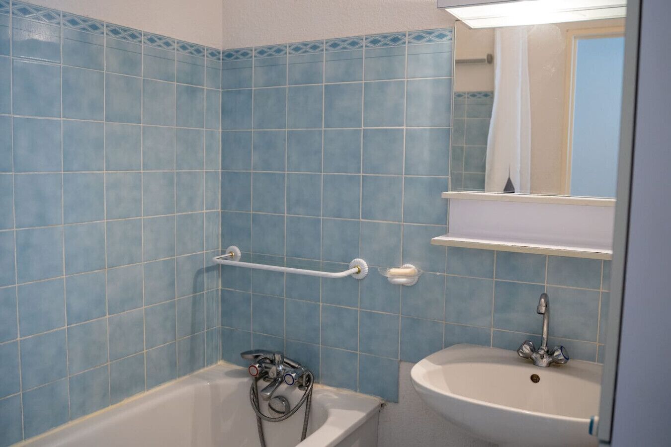 Un baño con azulejos azules, una bañera, un lavamanos y un perchero para toallas.