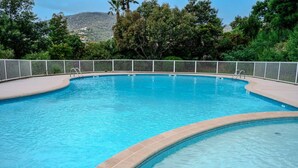 A clear blue swimming pool with a tiled edge, surrounded by a white fence and lush greenery.