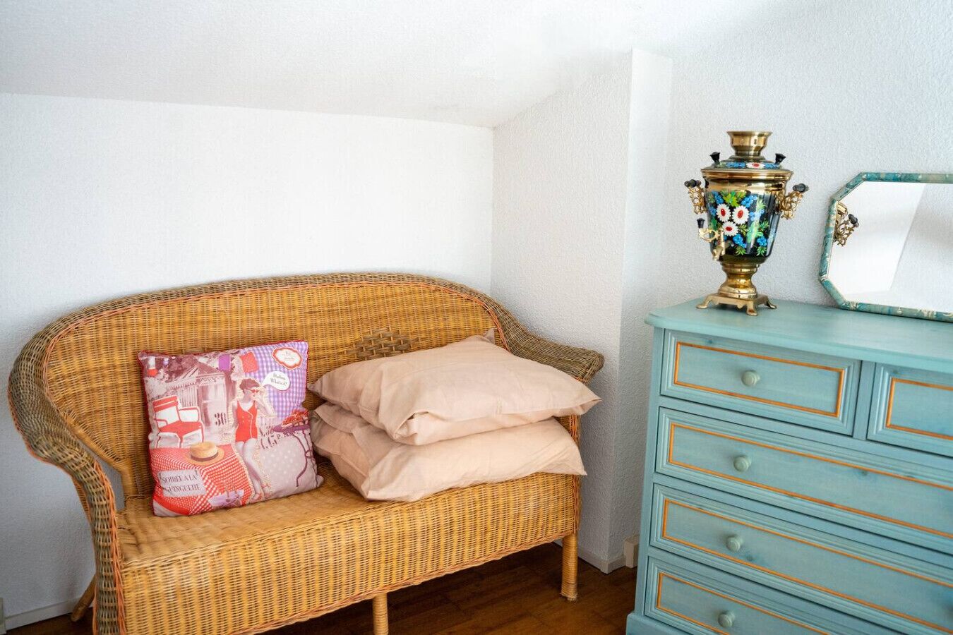 A wicker sofa with two pillows, a small decorative vase, and a mirror on a dresser.