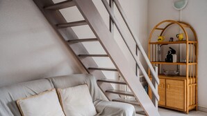 A staircase with a wooden railing, a white sofa with cushions, and a wicker side table with a lamp.