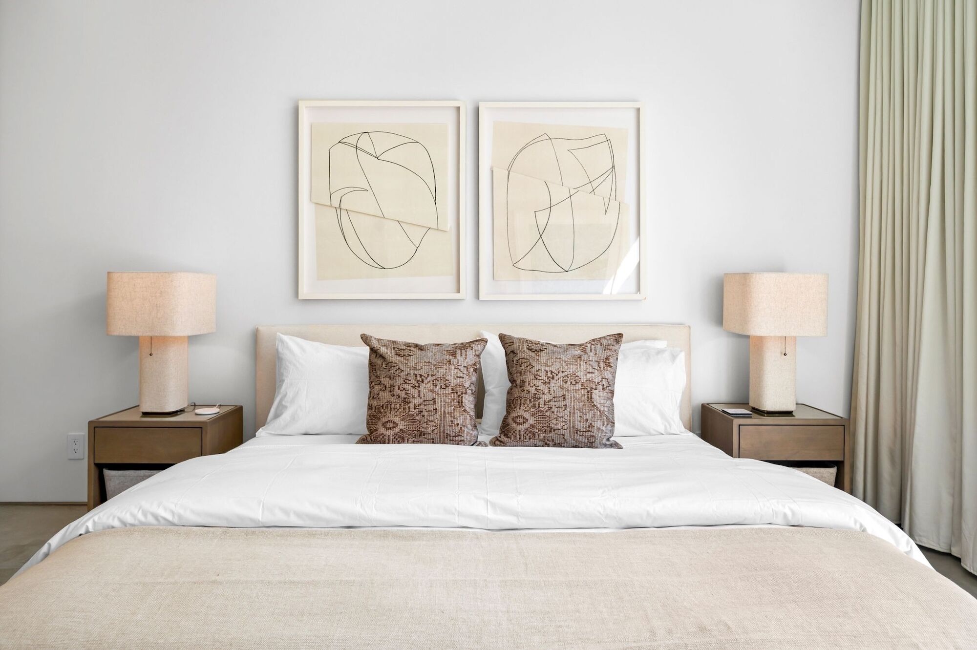 A neatly arranged hotel room with a large bed, two nightstands, two wall-mounted lamps, and two abstract artwork pieces.