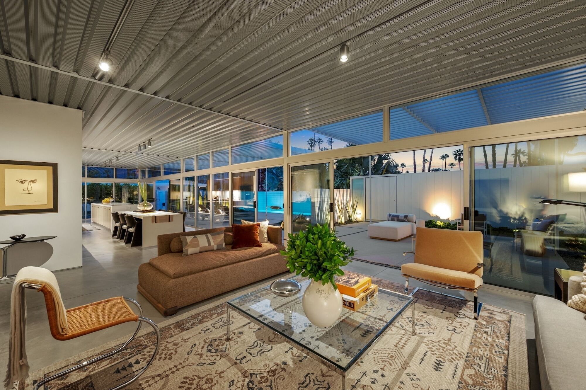 A modern living room with a sofa, armchairs, and a coffee table. There is a large window offering a view of the outdoors.