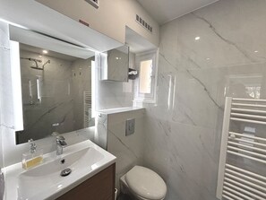 Une salle de bain moderne avec un mur en marbre, un grand miroir, un lavabo avec un distributeur de savon et des toilettes.