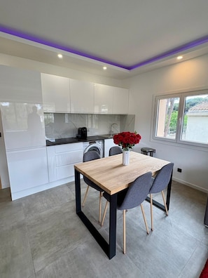 A modern kitchen with white cabinets, a wooden dining table, and a vase with red flowers.
