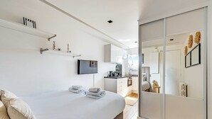 A modern hotel room with a bed, a TV, a kitchen area, and a sliding door closet. - Bright Studio - 2P - Arc de Triomphe (Paris)