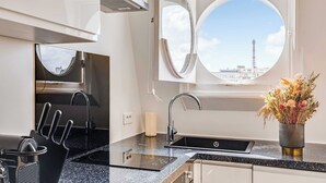 A kitchen with a round window, a sink, a vase with flowers, and a view of a tower. - Bright Studio - 2P - Arc de Triomphe (Paris)