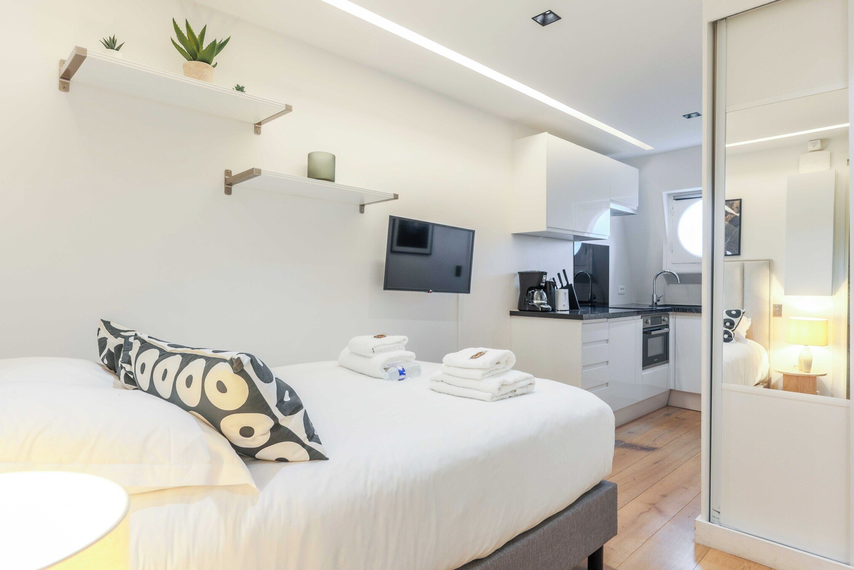 Ein modernes Hotelzimmer mit Bett, Nachttisch, Fernseher und einer Küchenzeile.