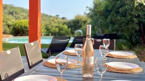 A table set outdoors with a bottle of wine, glasses, and plates on a wooden table. - Lou Tavan - Villa 4 Chambres - Piscine & Jacuzzi (Le Lavandou)