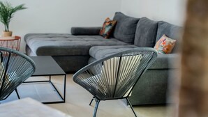 A modern living room with a grey sectional sofa, two black wireframe chairs, and a small round table. - Lou Tavan - Villa 4 Chambres - Piscine & Jacuzzi (Le Lavandou)