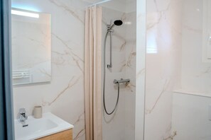 Ein Badezimmer mit einer gläsernen Duschkabine, einem weißen Waschbecken und einem Spiegel.