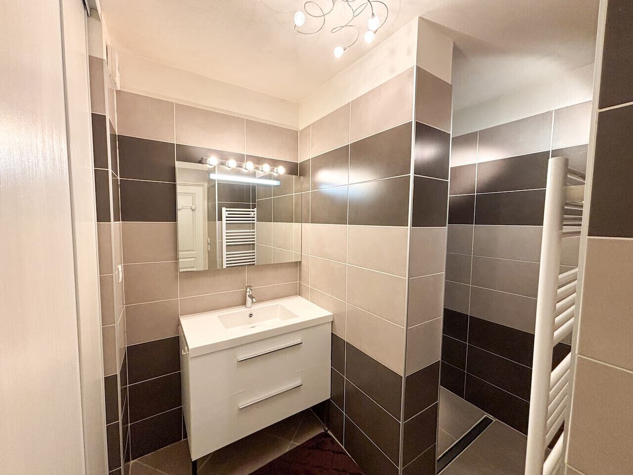 Un baño con lavamanos blanco, espejo y toallero.