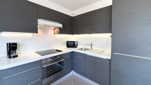 A modern kitchen with dark cabinetry, a built-in oven, a microwave, and a coffee maker.