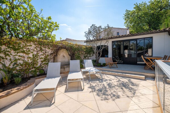 An outdoor patio with lounge chairs, a table, and a glass door leading to a covered area.