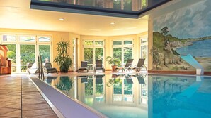 An indoor swimming pool with clear glass walls, lounge chairs, and a mural of a coastal landscape. - Seepark Heidenholz, Plau am See (Plau am See)