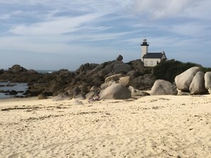 A beach with large rocks, a lighthouse, and a house in the background. - Guest Room in Lesneven (Lesneven)
