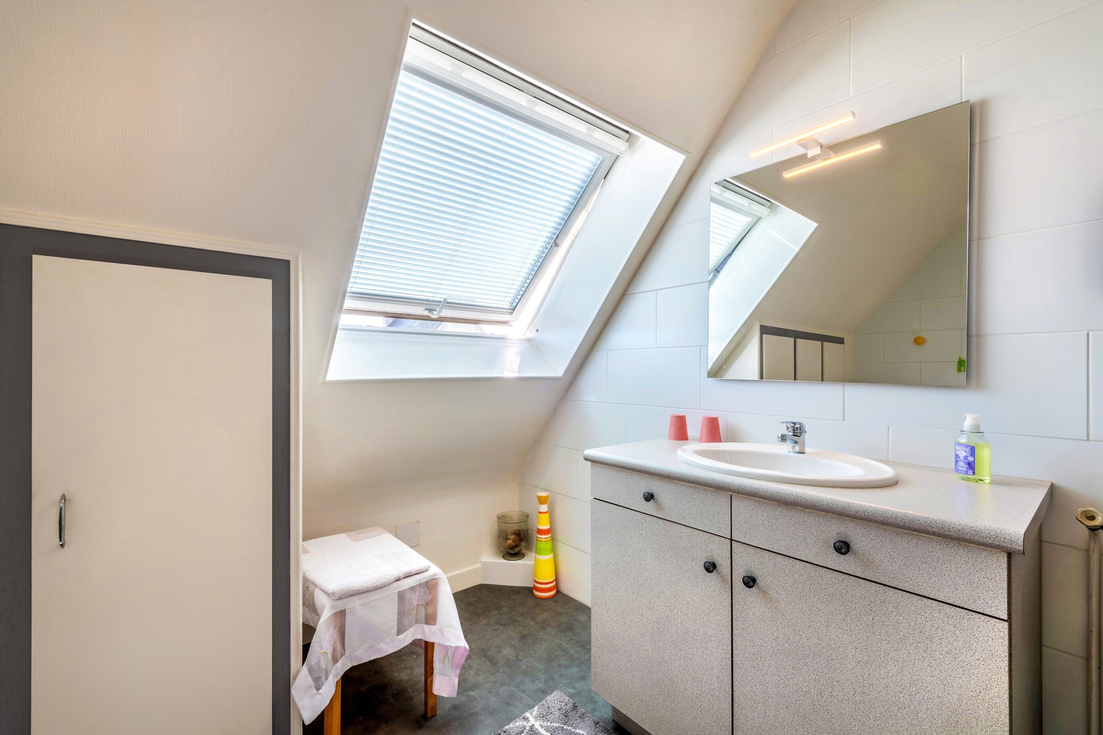 Een badkamer met dakraam, wastafel, spiegel en een klein tafeltje.