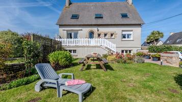 Une maison à deux étages avec une clôture blanche en bois, une terrasse en bois et une table de patio.