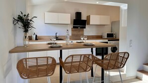 Una cocina moderna con encimera de madera, armarios blancos y tres sillas de mimbre.