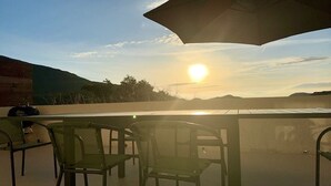 Un área de estar al aire libre con mesa y sillas, con vistas a un paisaje pintoresco y una puesta de sol.