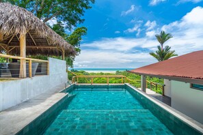 A swimming pool with a view of the ocean, a thatched-roof structure, and a red-roofed building. - Easy access with unparalleled views in Ojochal. Minutes to restaurants and beaches (Ojochal)