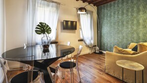 A dining area with a glass table and chairs, a large plant, a TV, and a sofa with cushions. - Lovely one bedroom near Signoria Square (Firenze)